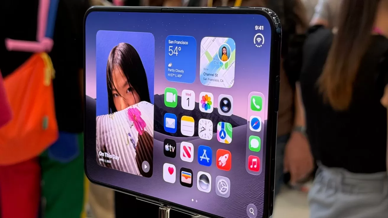 iPhone Duo on display, screen showing iPad-like home screen with app icons and photo widget, held upright in a busy indoor event with blurred people in background