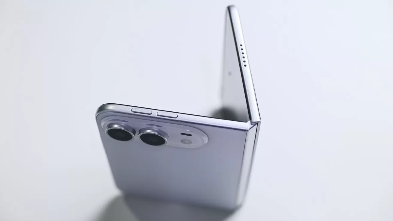 Silver foldable smartphone partially open on a light surface, showing dual rear cameras, side buttons, thin hinge, and upper speaker holes in a clean, minimalist setting