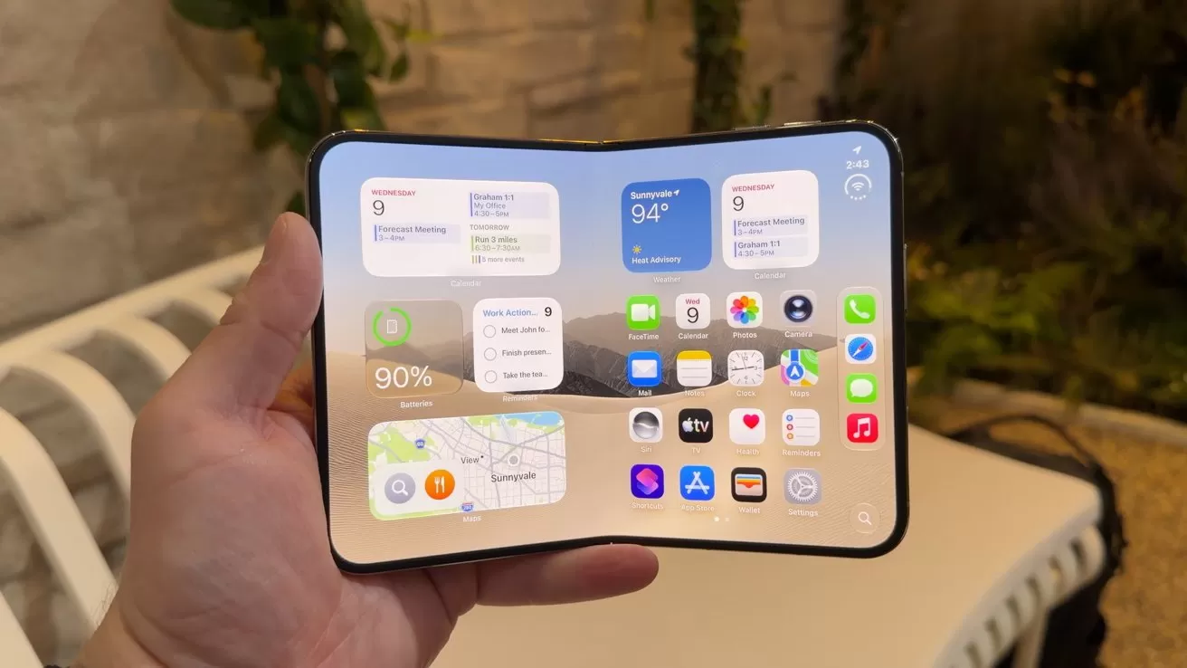 Hand holding a large foldable smartphone fully open, showing a bright home screen with multiple app icons and widgets, against an outdoor patio background with white furniture and green plants