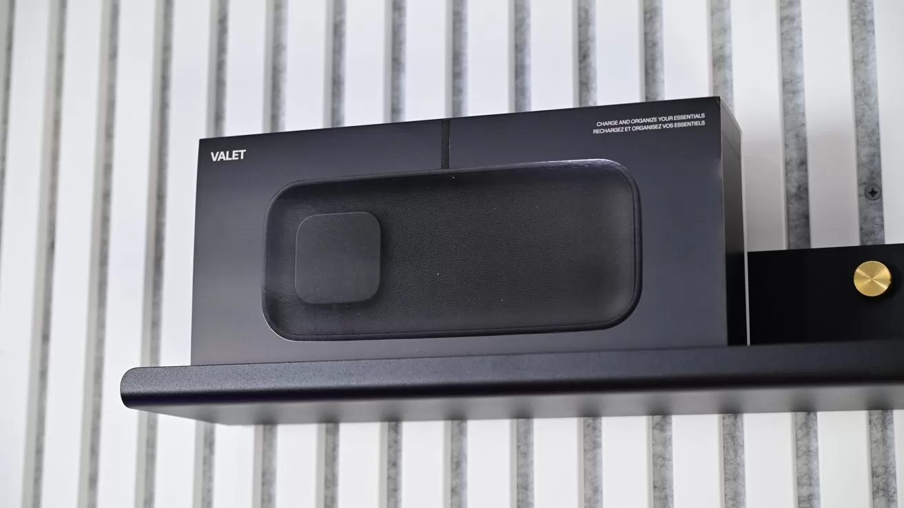 Black Valet-branded electronics box resting on a sleek black wall shelf, against a vertical white-and-gray striped wall background