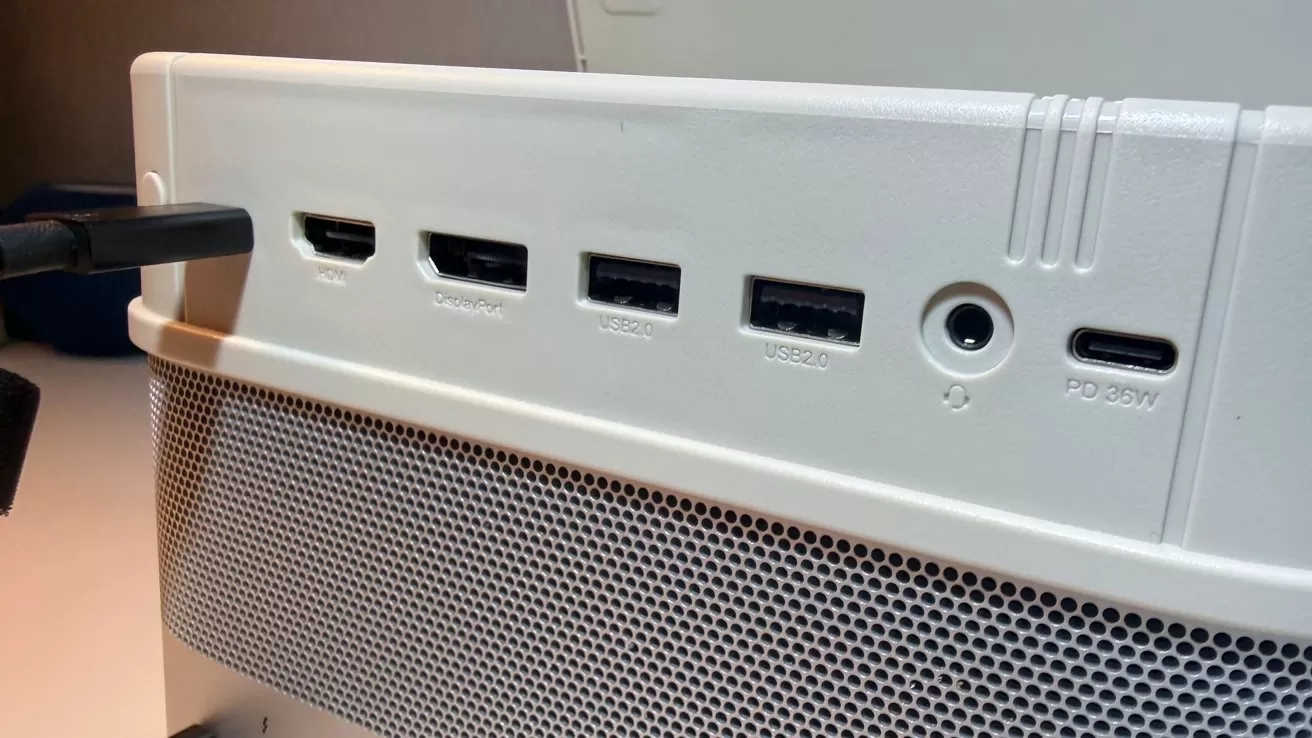 Close-up of a white computer monitor's back panel showing HDMI ports, two USB ports, a headphone jack, and a USB-C power port, above a perforated speaker grille