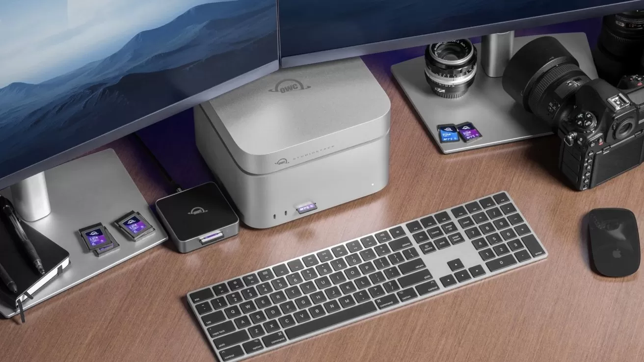Desk setup with dual monitors, a Mac Studio, keyboard, mouse, memory card readers, and professional camera equipment