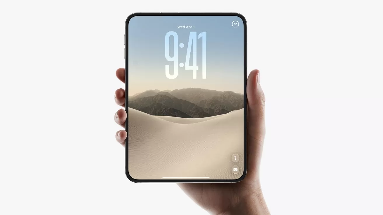 Hand holding a small tablet with thin black bezel, displaying a 9:41 lock screen over a desert sand dune and mountain landscape against a plain light background