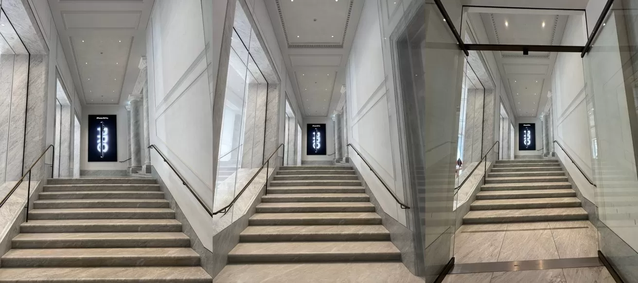 Wide marble staircase in a modern building, flanked by glass and white walls, with metal railings and a dark vertical sign glowing at the top landing