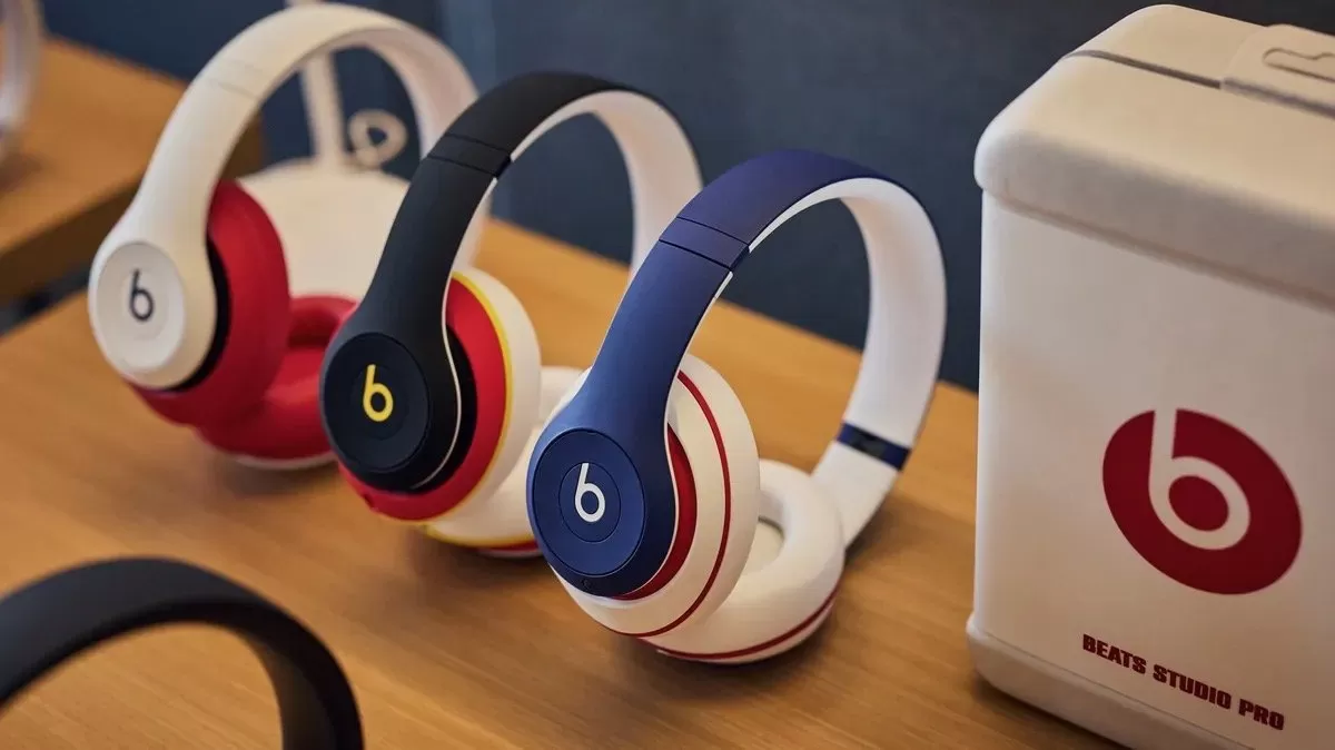 Three colorful Beats over-ear headphones on a wooden table beside a white Beats storage box, arranged neatly in a row, emphasizing modern design and bold branding