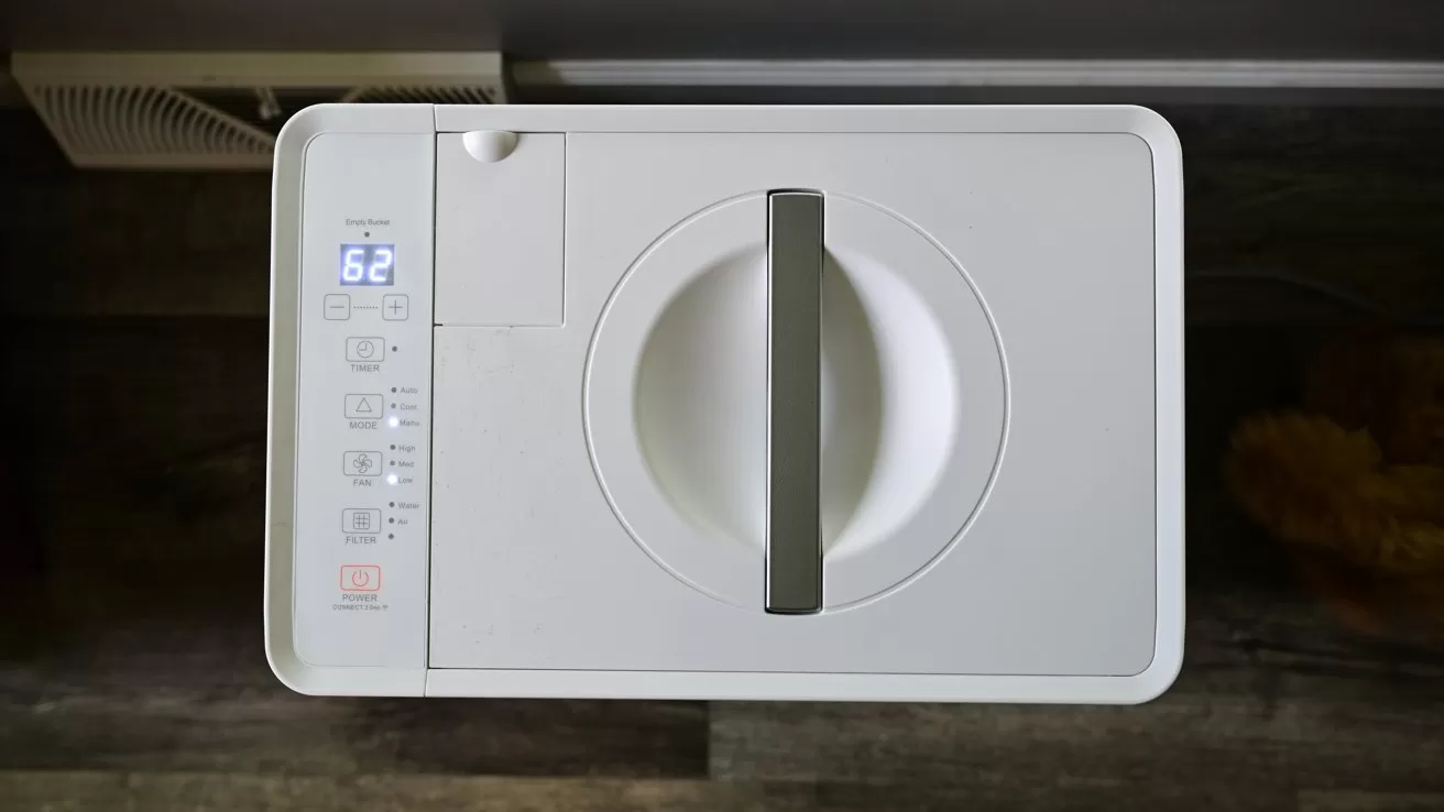 Top view of a compact white kitchen appliance with a central gray handle, digital display reading 62, and several touch buttons, placed on a dark wooden countertop