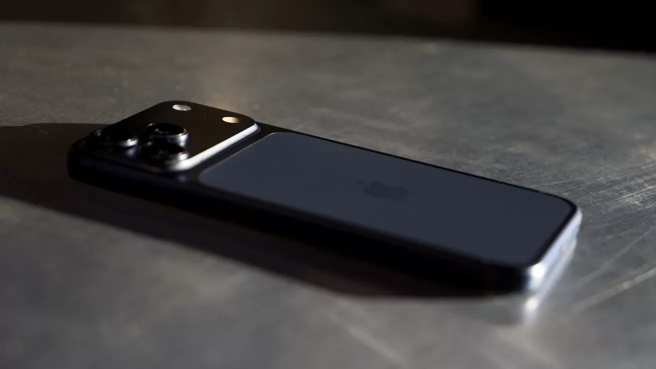 Black smartphone lying face down on a metallic surface, camera module with multiple lenses catching light, soft reflections emphasizing sleek, modern design