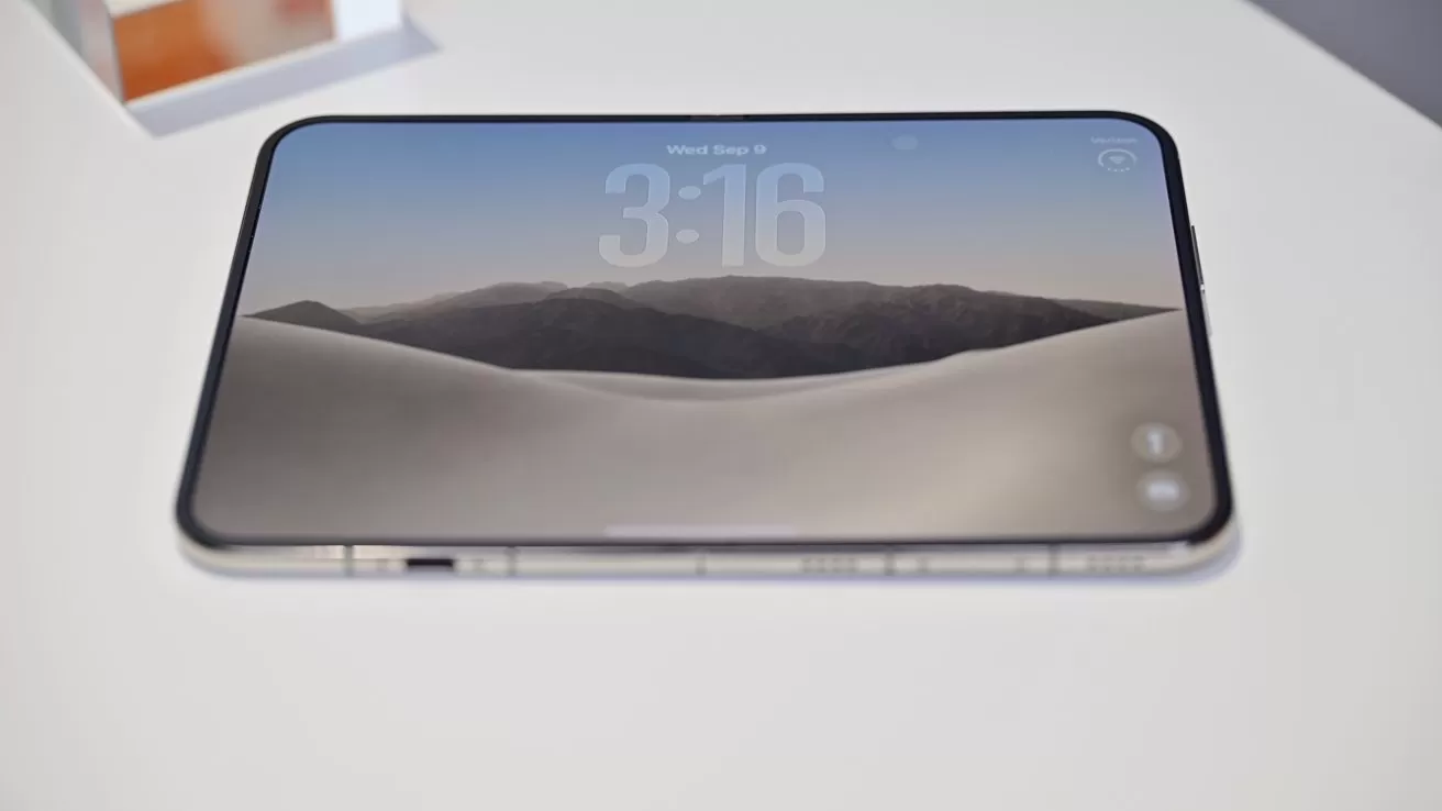 Smartphone lying flat on a white surface, screen on, displaying a minimalist desert landscape wallpaper with distant mountains and large digital clock reading 3:16 at the top