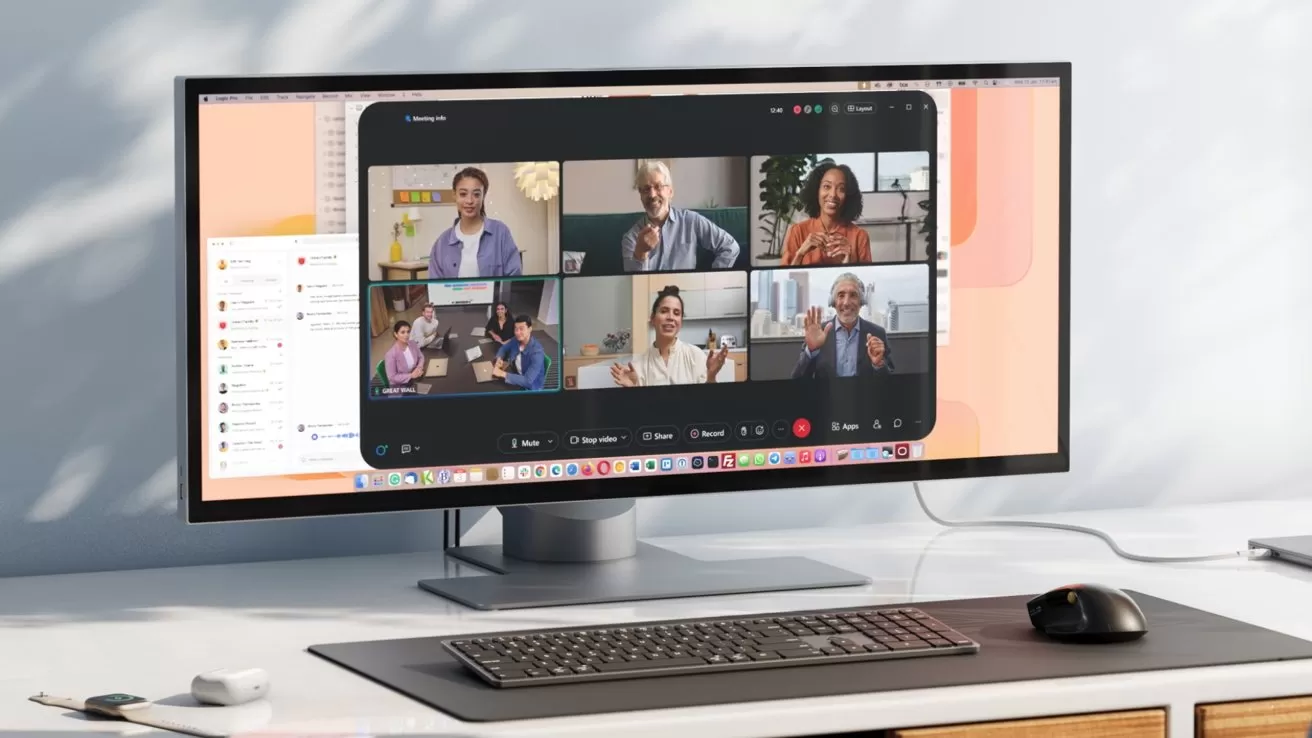Ultrawide monitor on a desk showing a video conference with six people in separate windows, with keyboard, mouse, and minimal office accessories arranged neatly in front