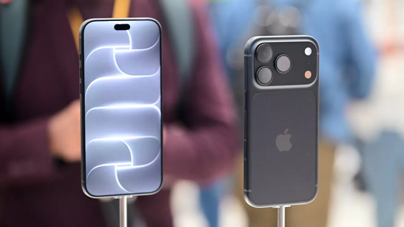 Two modern iPhones on display stands, one showing a bright abstract screen pattern, the other showing the back with triple cameras, against a blurred indoor background with people.