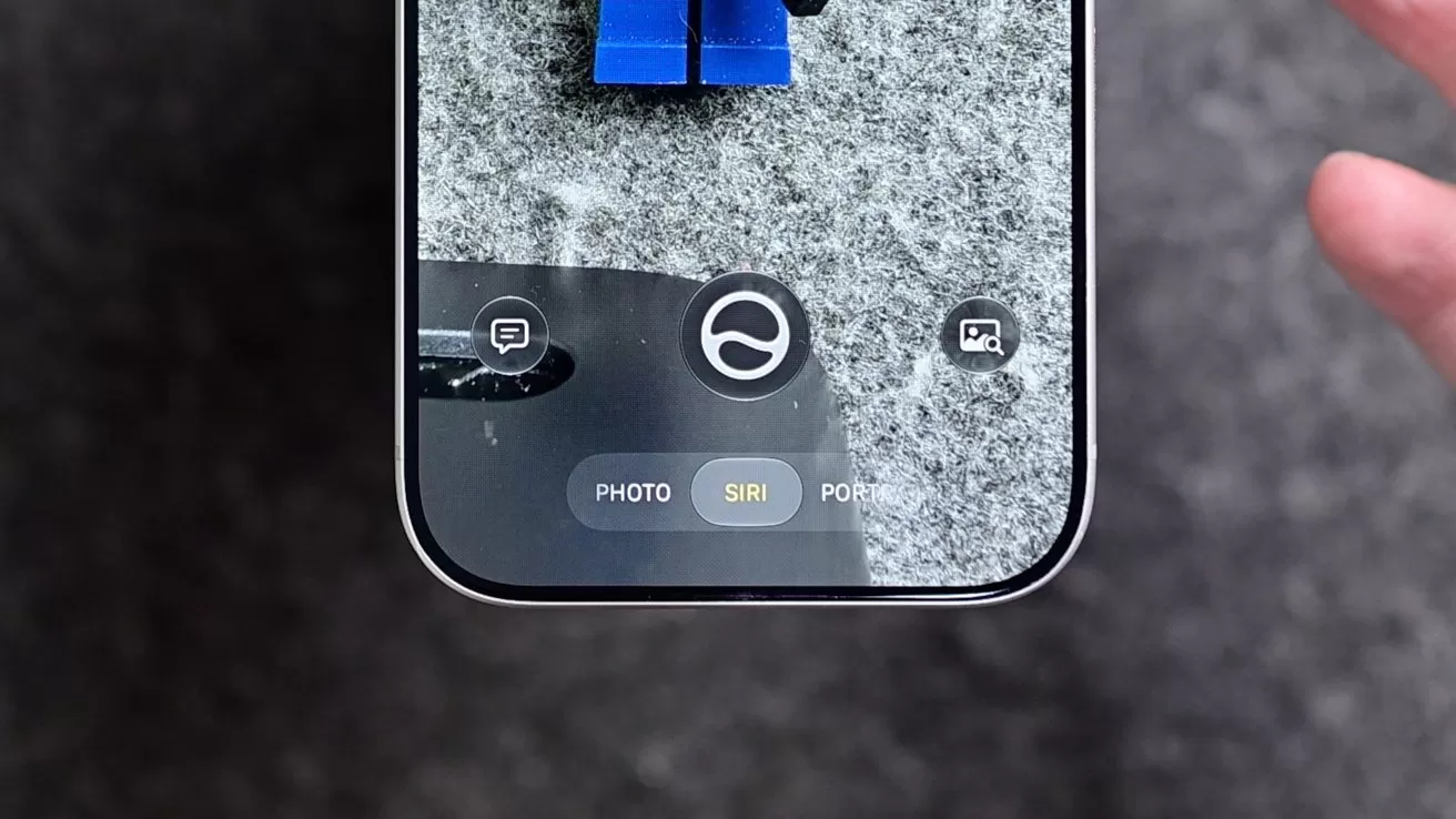 Close-up of a smartphone screen using camera app in Siri mode, focusing on blue toy legs on a gray surface, with a hand visible on the right edge