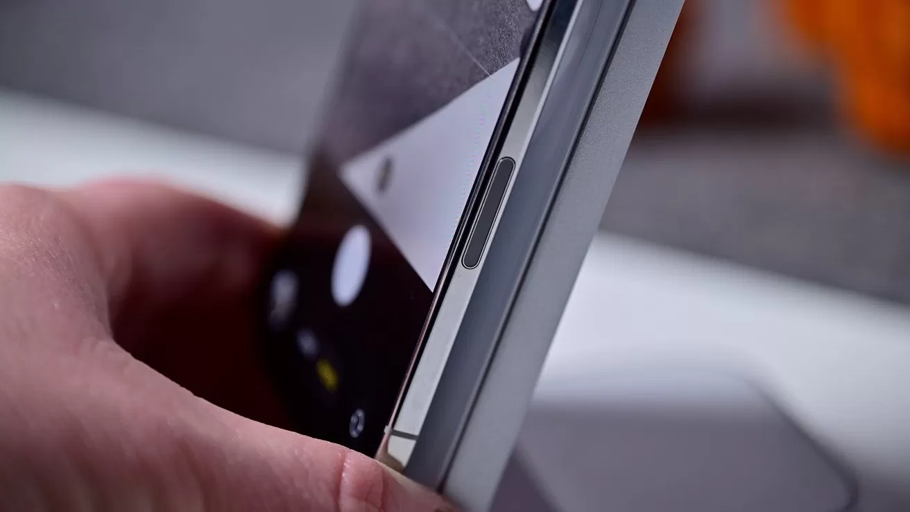 Person holding a smartphone with a focus on the side button and partially visible screen displaying a camera app.