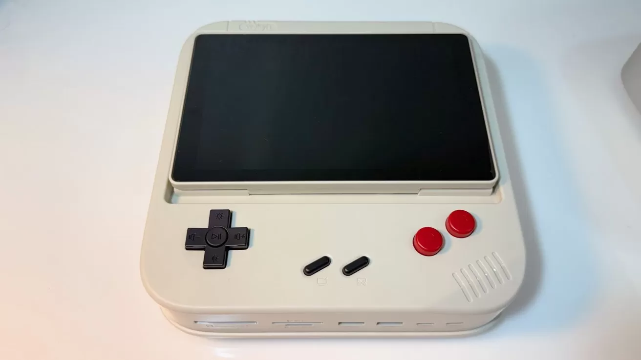 Retro-style handheld gaming console with a large black screen on top, beige body, black D-pad, two small black buttons, two red circular buttons, and speaker grille on the right