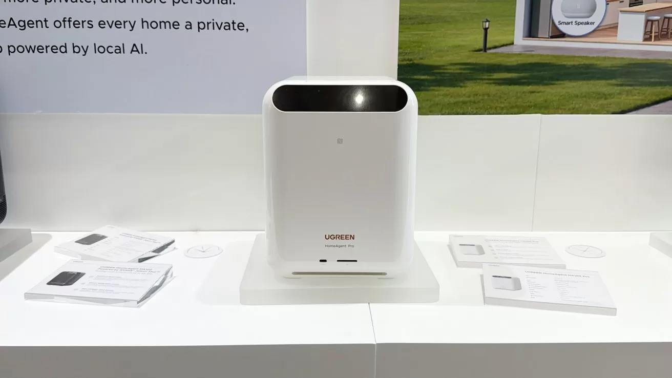 Sleek white rectangular tech device on a display table, with curved black top section, small logo reading Ugreen, and several product information sheets arranged around it in a well-lit booth.