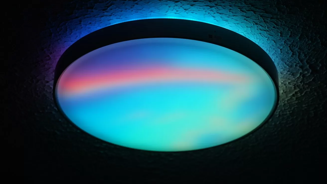 Round ceiling light glowing in soft gradients of blue, turquoise, and pink, casting colorful ambient light on the textured dark ceiling